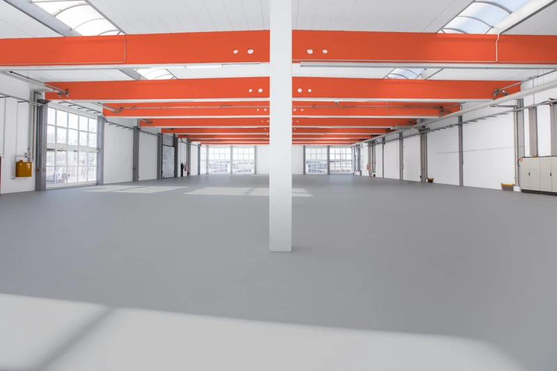 Der geräumige Innenraum einer frisch sanierten Industriehalle mit beschichtetem und dadurch robustem Betonboden.
