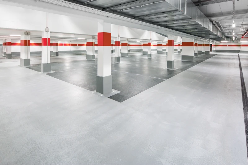 Innenansicht einer Parkgarage mit veredeltem Betonboden und vielen Säulen, die rote Markierungsstreifen haben.
