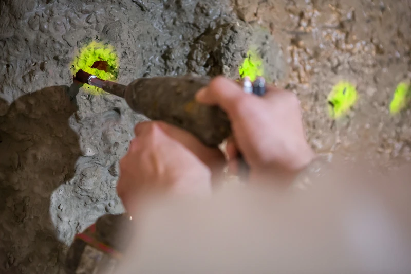 Ein Mitarbeiter der Resintech GmbH bohrt an mit gelber Leuchtfarbe markierten Stellen in eine Betonwand.