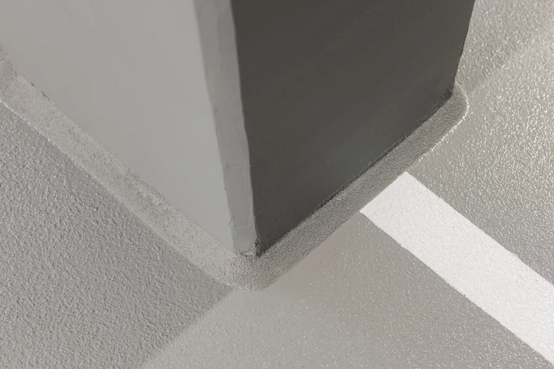 Nahaufnahme eines Betonpfeilers, der auf einem frisch beschichteten Betonboden mit weißer Parkplatzmarkierung in einer Tiefgarage steht.