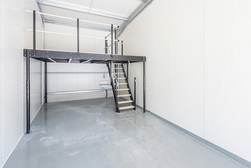 Ein Lagerraum mit einer kleinen Galerie und Treppe. Der Fußboden aus Beton ist frisch beschichtet und die Innenwände sauber in weiß gestrichen.
